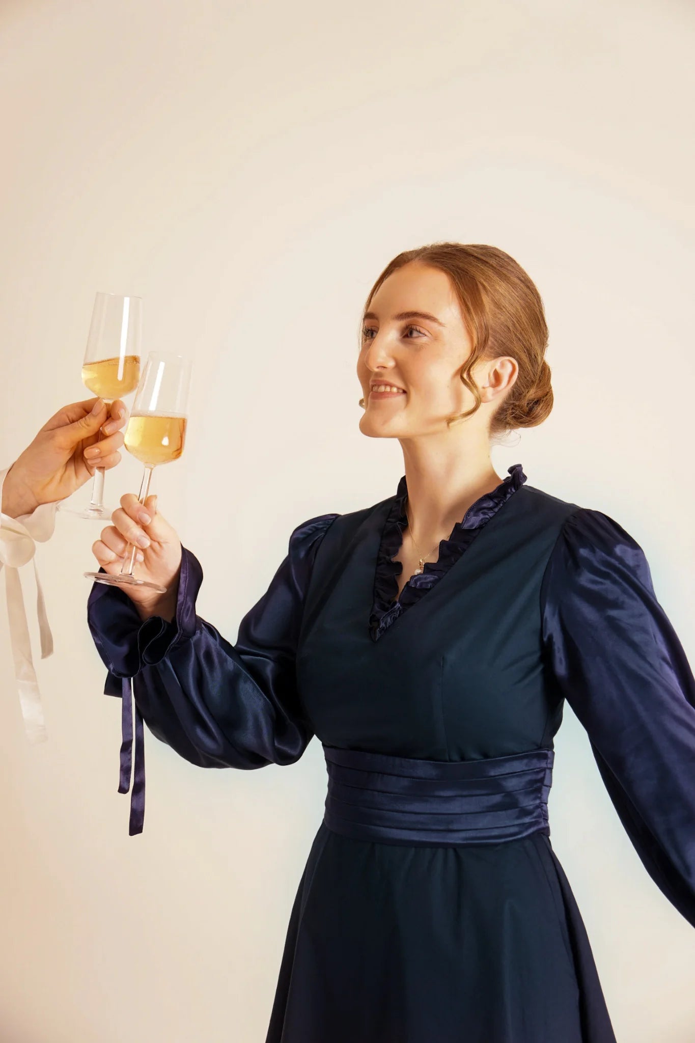 Woman in a dark blue dress holding a glass of champagne against a plain background