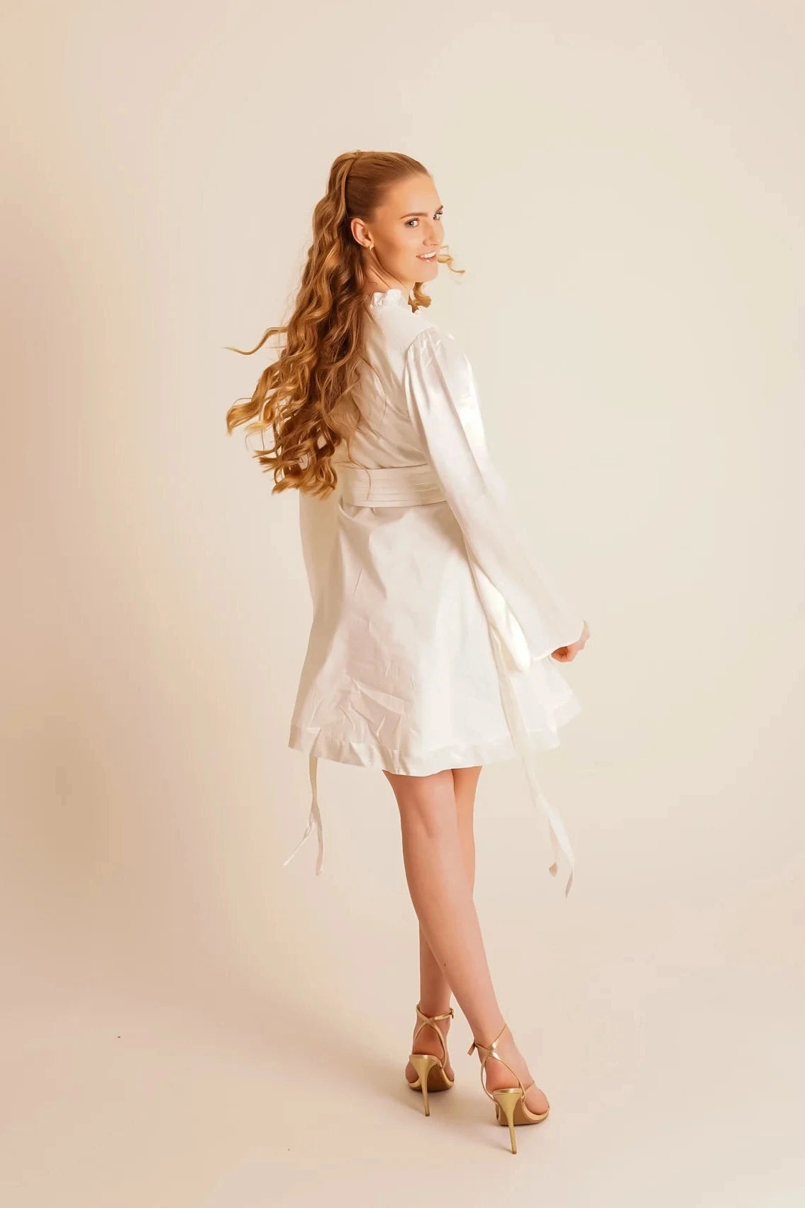 Woman wearing a white dress with long sleeves against a beige background