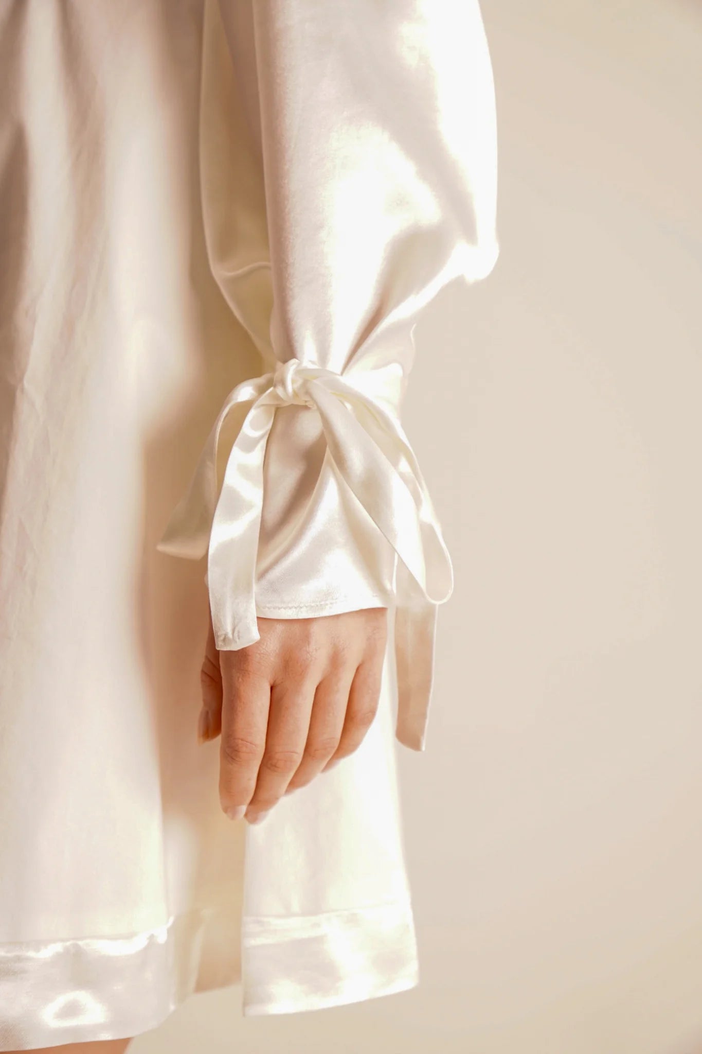 Close-up of a white satin robe with a hand wearing a ring, on a plain background.