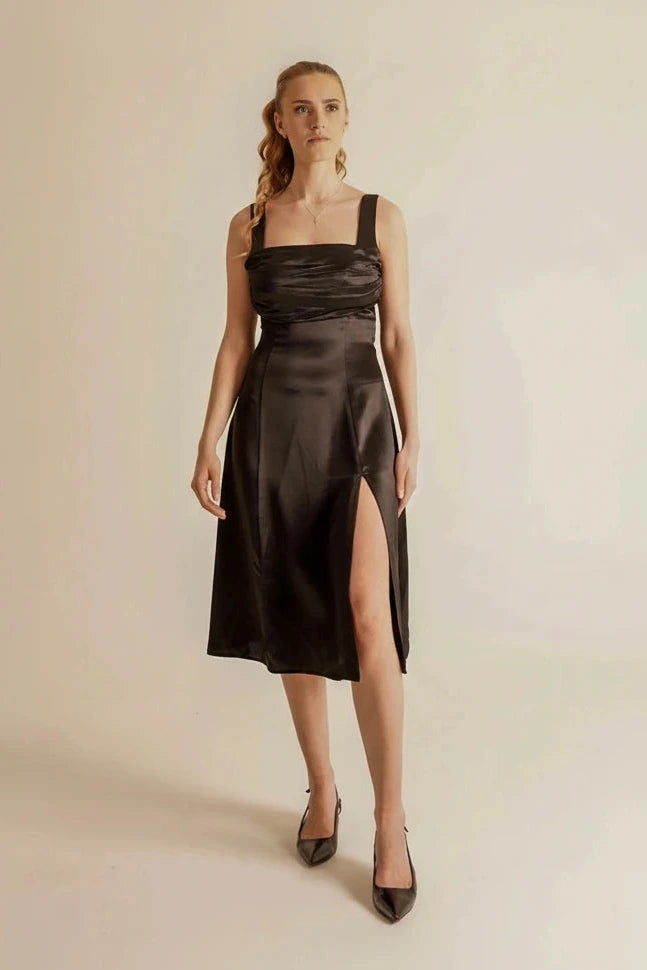 Woman wearing a black satin dress with a slit on a beige background